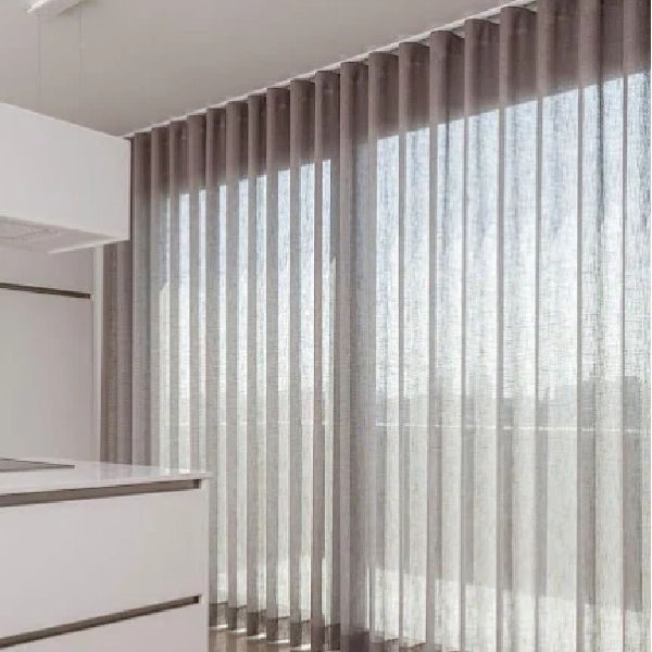 A light-colored, sheer wave-fold curtain covering a large window, with sunlight filtering through.