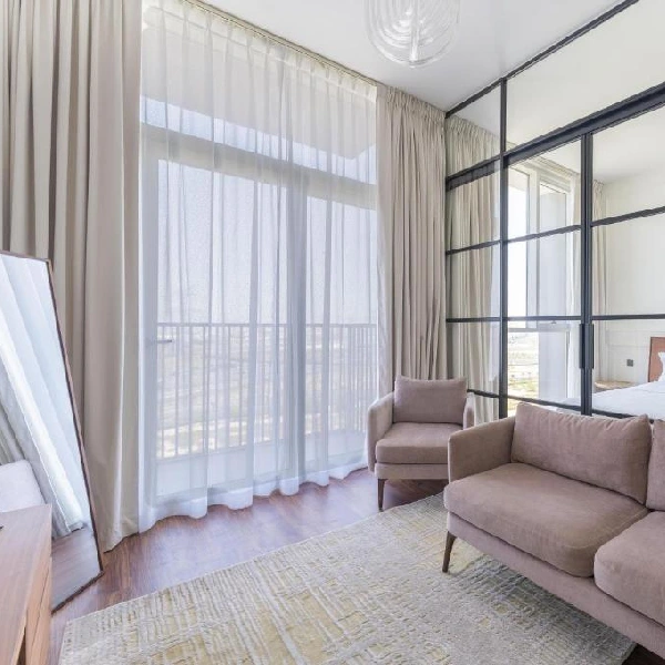 Beige opaque curtains are drawn to the sides, revealing a sheer white curtain covering a large window that overlooks a balcony