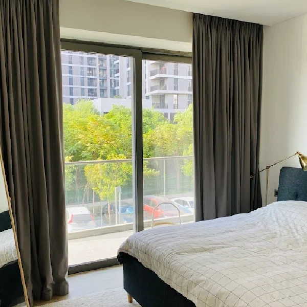 Dark grey curtains frame a balcony door with a view of green trees and buildings.