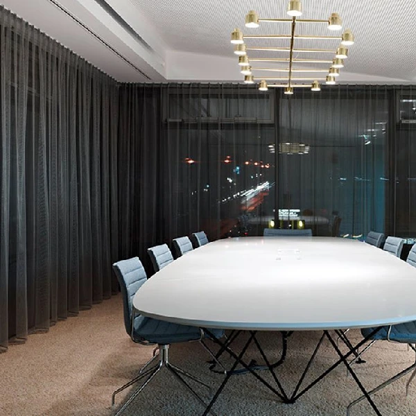 Dark sheer curtains in a modern conference room with a large white oval table and blue chairs.