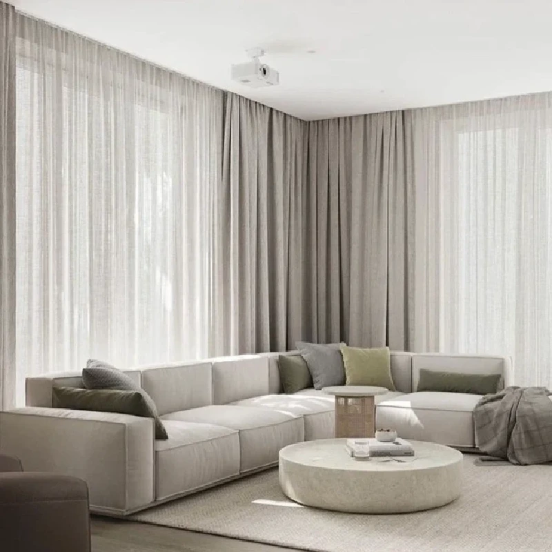 Grey and sheer white motorized curtains framing a living room with a large white sectional sofa and throw pillows.