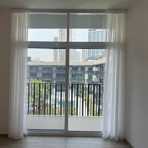 White sheer curtains framing a balcony view of modern buildings and a pool area.