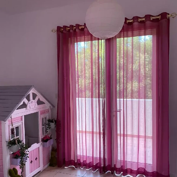 sheer curtains hang over a window, revealing trees outside