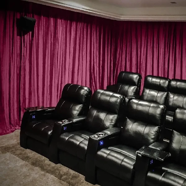 Burgundy theater curtains behind rows of black recliners in a home cinema.